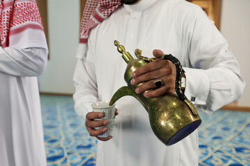 Arab man holding Dallah and pours Arabic coffee to guests