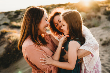 Three generations women happy kissing hugging beach summer sunset