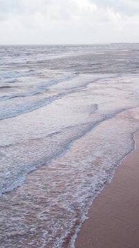 Vertical Aerial view of tropical sandy beach at Mandvi, Kutch, India. Beach waves and clouds in sky during monsoon season. Bird Eye View 4K Cinematic Drone Footage. Travel and holidays concept.
