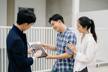 Asian man Real estate broker agent showing a house detail in her file to the young Asian couple lover looking and interest to buy it.