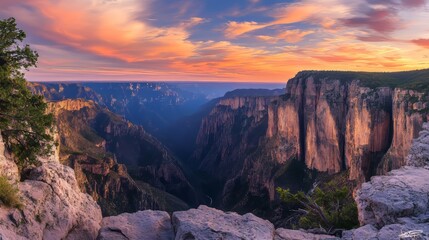 Fototapeta premium Panoramic View of Rugged Mountain Landscape at Sunset, Dramatic Cliffs and Deep Gorges with Sky Ablaze in Warm Hues of Orange and Pink