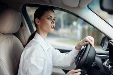 Woman driving car, hand on steering wheel, surprised expression at camera, wearing white shirt