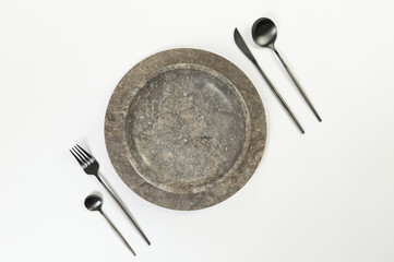 Top view of brown marble tray and plate, black cutlery on white background. Food presentation, stone tray. Table setting, copy space, flat lay.