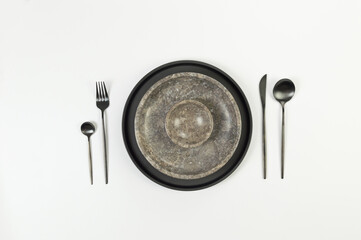 Top view of brown marble plate and bowl, black plate and cutlery on white background. Food presentation, stone tray. Table setting, copy space, flat lay.