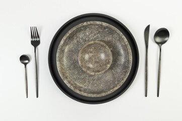Top view of brown marble plate and bowl, black plate and cutlery on white background. Food presentation, stone tray. Table setting, copy space, flat lay.