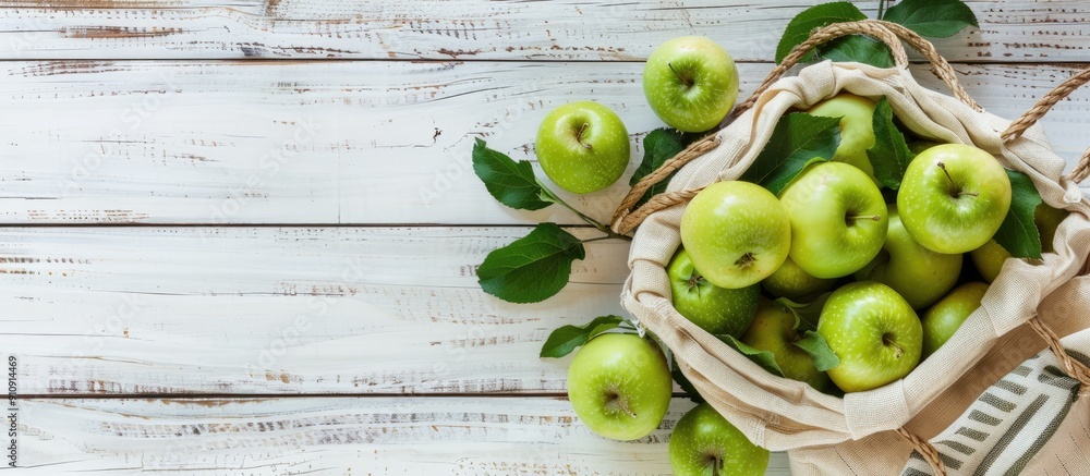 Poster Eco friendly bag with green apples on white wooden backdrop showcasing sustainable living with zero waste practices Top down view with ample copy space image