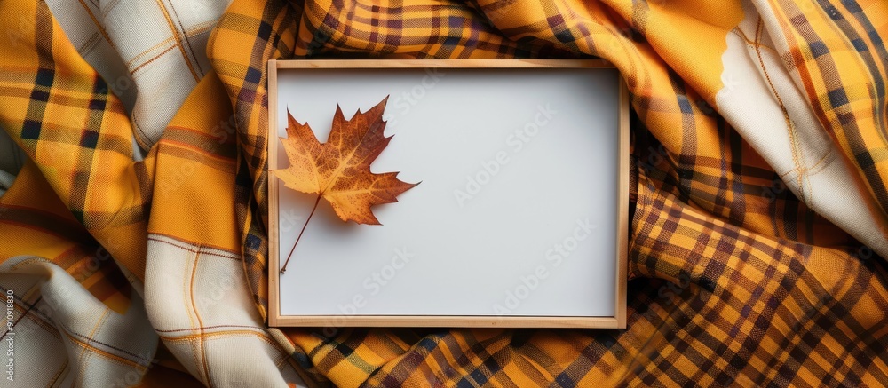 Leinwandbilder Top view of an empty white board surrounded by autumn themed elements like a maple leaf on a checkered yellow scarf perfect for a copy space image