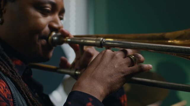 Close up view of African American musician playing trombone during rehearsal with band, male drummer in background