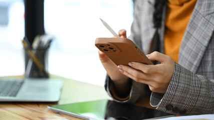 Close up shot of young woman taking break from work and checking social media on her mobile phone