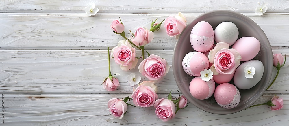Poster Top view image of Easter eggs in pink and grey hues in a gray dish adorned with roses set on a rustic white wooden table with copy space image