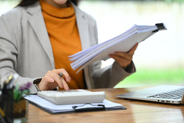 Businesswoman holding a stack of documents and using a calculator at her workplace