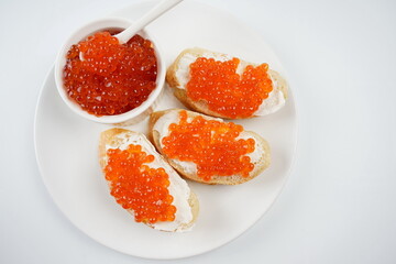 Slices of bread with red caviar on white plate and red fish caviar on a spoon in a bowl