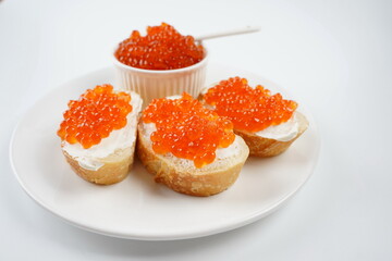 Slices of bread with red caviar on white plate and red fish caviar on a spoon in a bowl