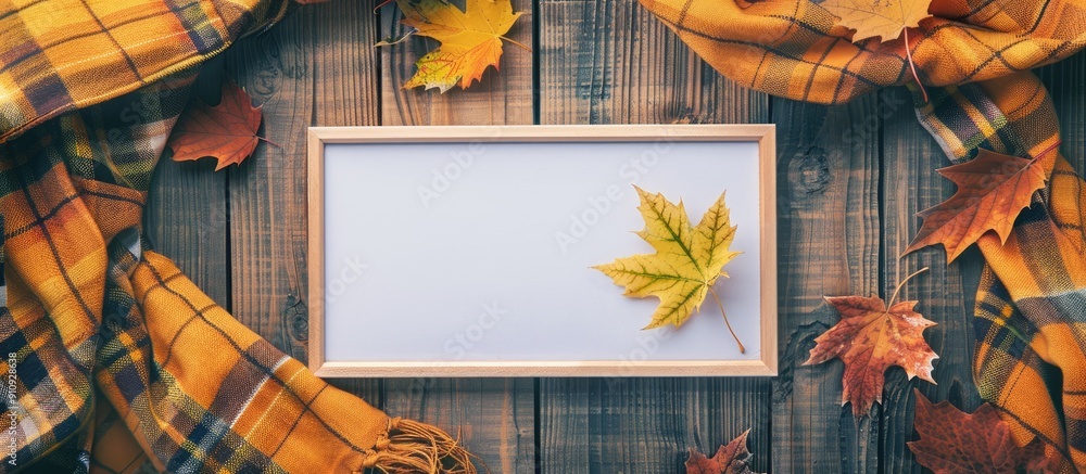 Poster Top view of an empty white board surrounded by autumn themed elements like a maple leaf on a checkered yellow scarf perfect for a copy space image