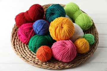 Pile of different yarns and wicker mat on white wooden table