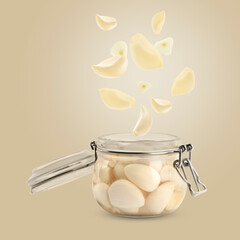 Jar with pickled garlic and cloves falling into it on dark beige background