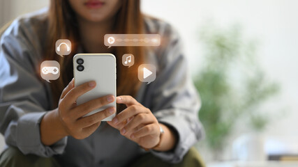 Young woman using smartphone, interacting with various multimedia icons including music, video and...