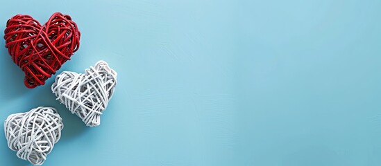 Fototapeta premium Valentine s Day themed flat lay featuring white rattan hearts with a red heart on a blue background ideal for a greeting card with copy space image