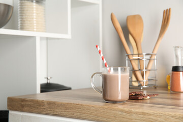 Glass cup of sweet chocolate milk on wooden table in kitchen