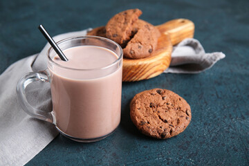Glass cup of sweet chocolate milk and wooden board with tasty cookies on dark background