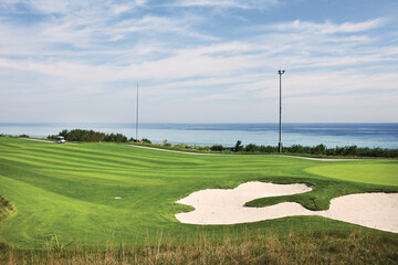 Obraz premium 푸른하늘에 녹색잔디가 있고 바다가 보이는 골프장풍경.