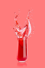 Red cherry juice in drinking glass with bright splashes, drops flying, swirl on pink background. Organic summer berries beverage with splashing for advertising, design, flyer, card, poster.