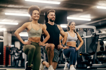 Happy group of sportspeople kneeling with hands on hips at gym.