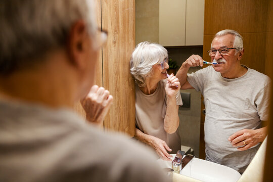 Mirror reflection of a morning senior couple brushing their teeth in bathroom together.