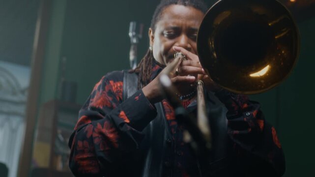 Rack focus shot of African American artist playing trombone in music studio while rehearsing with bandmates