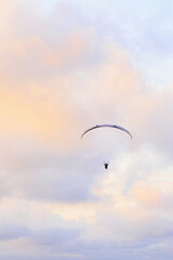 A paraglider flies in the blue pink cloudy sky at sunset. Fly on parachute, high-performance wing. Adventure sport of flying paragliders. Gran Alacant, Alicante, Spain