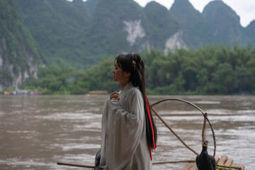Hanfu girl standing in Li River with Cormorant fishing bird perched on bamboo raft