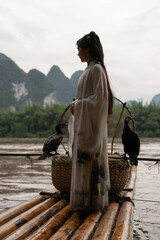 Chinese Hanfu girl fixing her hair while standing on bamboo raft by Li river, Xingping