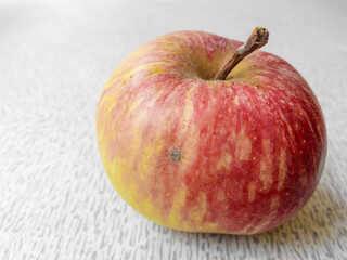 A wild ripe apple with red and yellow sides lies on the table. Details are visible. Close view