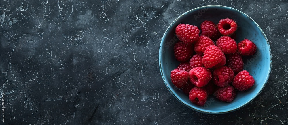 Poster Top down view of ripe raspberries in a blue bowl on a rugged black backdrop with space for text or images in the scene. copy space available