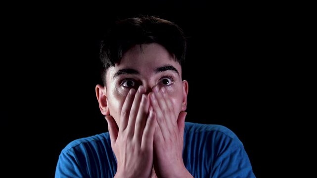 Shocked, terrified young man isolated on black background.