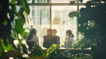 A meeting in a lush, plant-filled room bathed in sunlight, where four professionals engage in discussion, representing sustainable and green business practices.