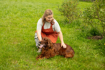 Cheerful happy young woman playing with her dog in the yard of the house in summer. Beautiful Irish...