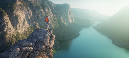 Naklejka premium Hiker on mountain peak watching river flow through rocks.