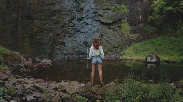 Traveler is enjoying the peaceful atmosphere of a hidden waterfall in a lush tropical forest during her adventure trip in french polynesia