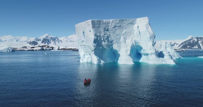 People boat tour expedition to Antarctic iceberg. Antarctica travel and exploration. Arctic winter glacier drift ocean. Pristine South Pole landscape, sunny day. Aerial drone flight panoramic zoom out