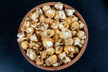 top view of pile of popcorn in wooden bowl on dark table