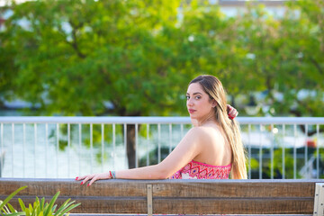 Young, pretty, blonde Spanish woman resting on a bench with her back facing backwards, the woman is...