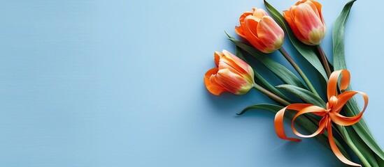 Obraz premium Greeting card featuring an orange tulips bouquet with ribbon on a light blue backdrop, ideal for a copy space image.