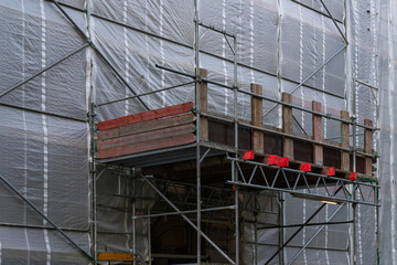 A wooden platform sits atop metal scaffolding, covered in protective sheeting, indicating ongoing construction and renovation efforts in the city.