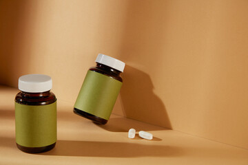 Medicine advertising mockup was shot from high angle with two blank green label medicine bottle. One leaning on yellow wall, the other standing on the flat, next to two white drug tablets