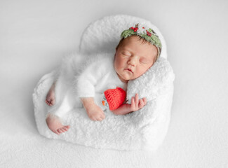 Newborn Girl Sleeps In Chair With Christmas Decorations During Baby Photo Session In Studio