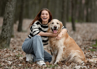 Teenage Girl Sits With Golden Retriever In Park During Autumn