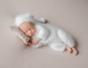 Newborn Baby In White Jumpsuit Sleeps During Studio Photoshoot
