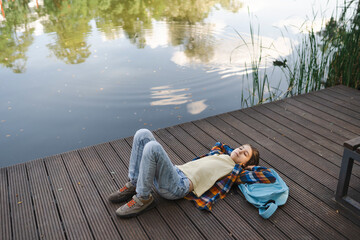 Boy lying on back and relaxing on pier near lake