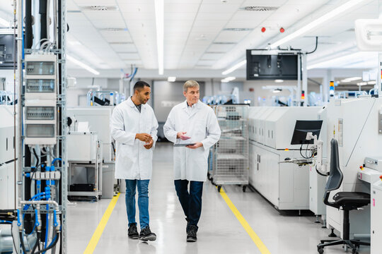 Two electrical technicians walking through factory workshop discussing over digital tablet
